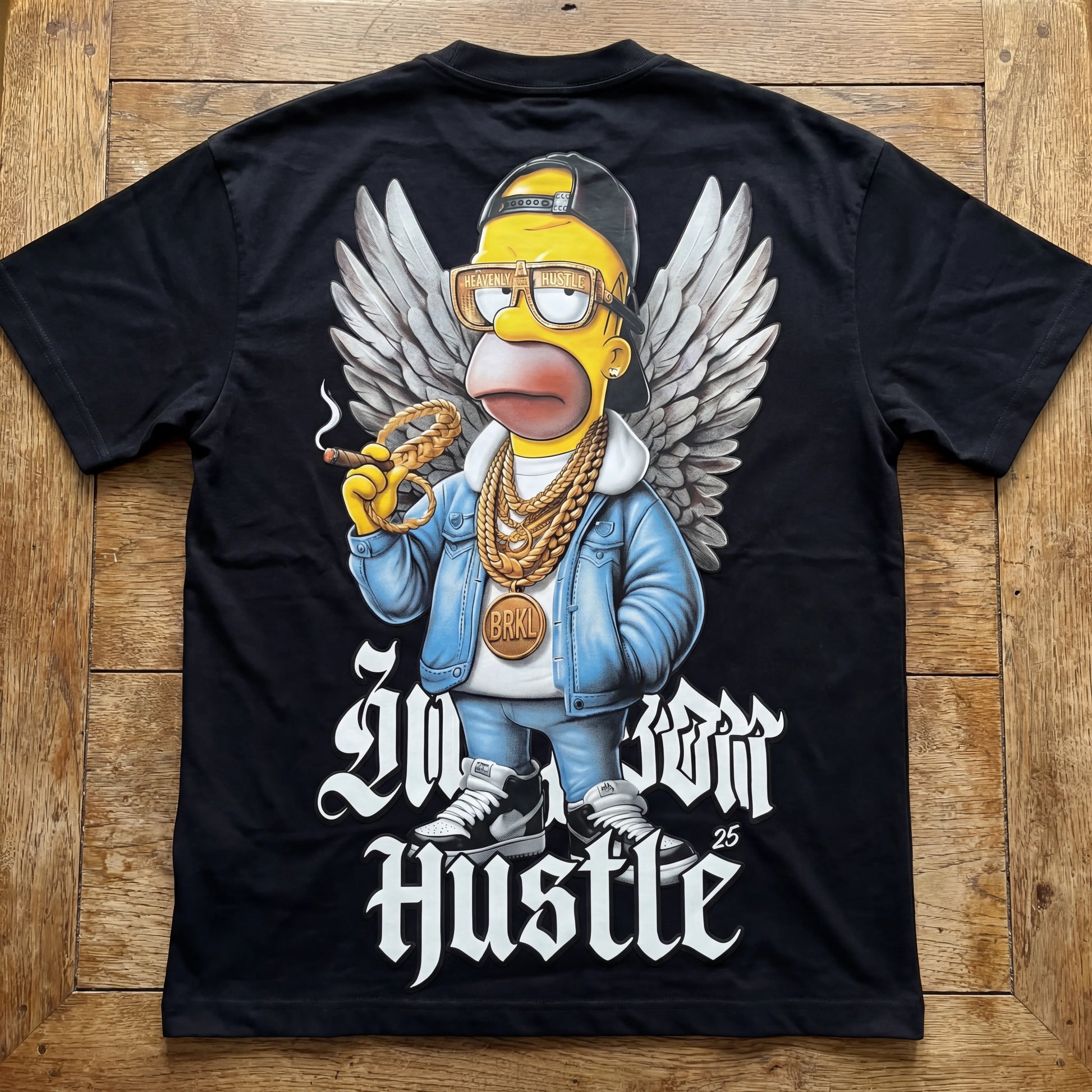 Black t-shirt with a graphic of a character wearing a blue jacket, gold chains, and sneakers on a wooden surface.